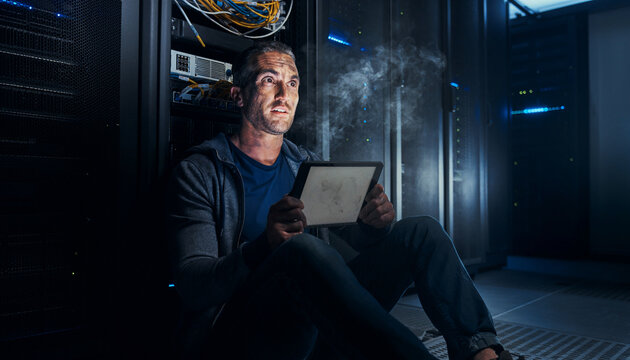IT specialist sits on the floor of a dark server room while dealing with a data center crash