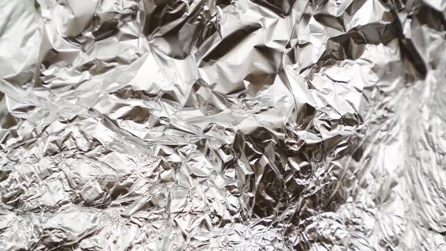 Crumpled aluminum foil surface moving and reflecting light. Abstract metallic texture background footage with shiny wrinkles and folds. Industrial material and packaging concept for design, wallpaper 