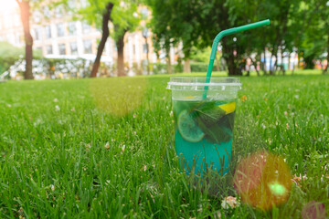 Refreshing blue lagoon cocktail or mojito drink with lime slice and mint leaves in a plastic takeaway cup with straw on vibrant green grass © Oleksandr Baranov