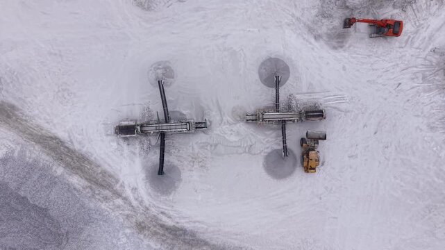 Top-down view of two mobile screener units positioned in a white gypsum quarry. One unit is being loaded by an orange excavator, a yellow loader visible nearby 