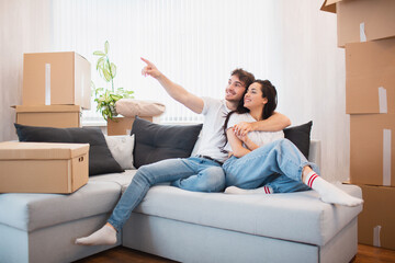 Obraz premium a happy young married couple moves to new apartment. They are sitting on the sofa and looking at their new home.