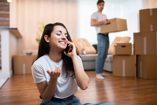 Moving and relationship concept. He is not satisfied. The husband unpacks the boxes. And the wife meanwhile does nothing. She prefers to talk to her friends. The husband is not satisfied.