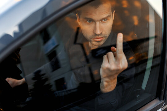 Angry man driving a car. Businessman shows middle finger in a car glass. A difficult situation on the road. High traffic