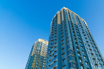 Obraz premium High-rise apartment buildings under clean blue sky, modern residential complex with contemporary glass facade panels and copy space
