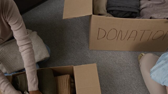 High angle shot of Black young woman and anonymous Caucasian boyfriend packing clothing items into donation boxes