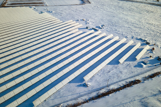 Aerial view of sustainable electrical power plant with solar photovoltaic panels covered with snow in winter for producing clean energy. Concept of low effectivity of renewable electricity in north