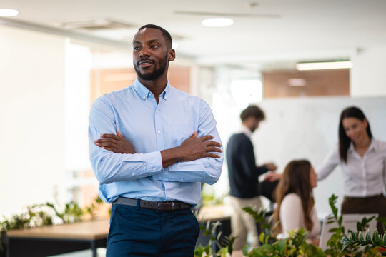 Confident black businessman standing arms crossed in modern office