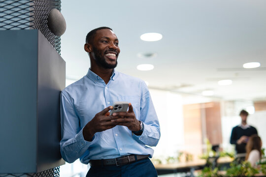 Black entrepreneur smiling while using smartphone in modern office