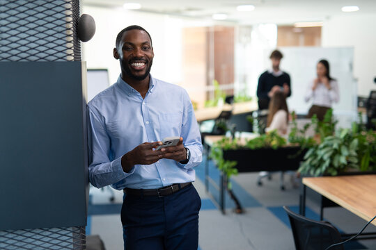 African american man smiling using smartphone in modern office