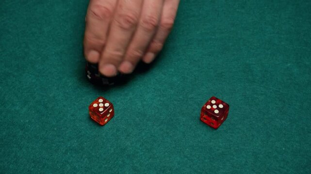 Hand places stack of poker chips on a green felt table next to two red dice during a game of chance in a casino setting