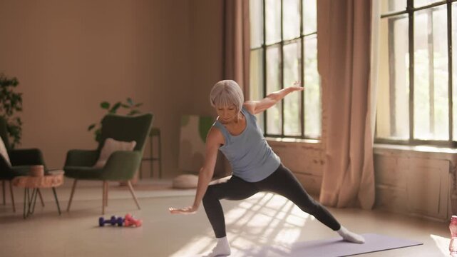 Woman in her 60s practicing triangle pose on fitness mat during yoga session