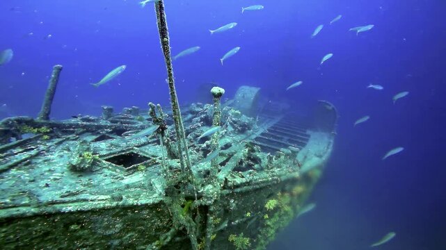 Underwater Descent to Shipwreck on Sandy Sea Floor Slow Motion. Cinematic underwater camera shot of descent towards a massive, rusted shipwreck sitting upright on a sandy ocean floor in deep blue sea.