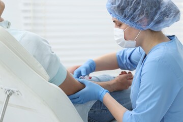Fototapeta premium Nurse drawing blood sample of patient's vein with syringe in clinic
