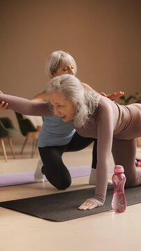 Female yoga coach assisting woman with balancing table pose during training