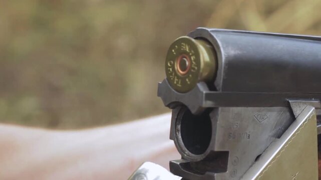 close up shot of a person loading two red shotgun shells into a double barrel shotgun outdoors