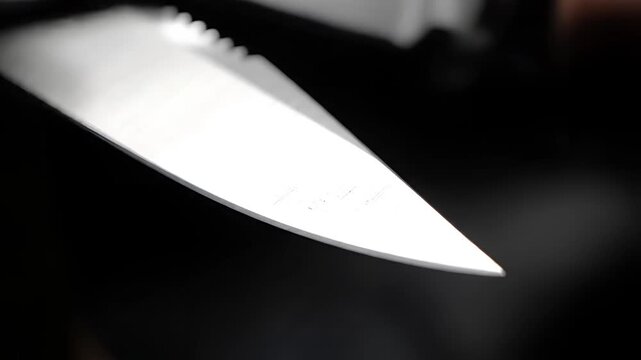 Closeup of a sharp knife blade reflecting light against a dark background.