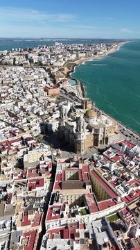 Aerial view of Cadiz Cathedral and its iconic golden dome by the sea. Cinematic drone shot of the historic landmark and the Atlantic Ocean coastline in Andalusia, Spain