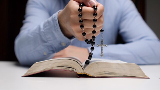 Hand holding rosary beads with crucifix over open bible, close up evoking faith, prayer and devotion in quiet reflection and spiritual connection to christian tradition and hope