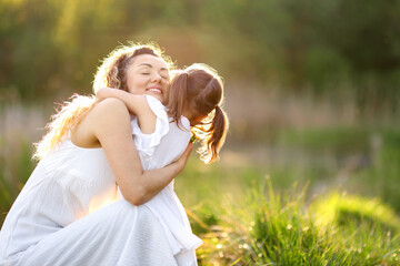 Fototapeta premium Mother hugging her cute little daughter in nature on sunny day. Space for text
