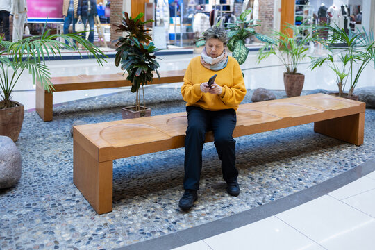 Mature woman in yellow sweater speaking on mobile phone, gesturing with hand, emotional conversation in modern interior.