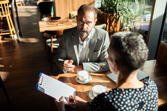 Senior businessman and woman discussing contract in cafe