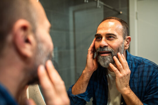 Middle-aged man checking beard in bathroom mirror