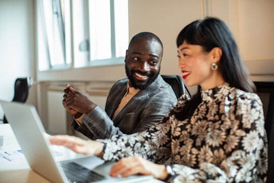 Smiling coworkers collaborating on laptop in modern office