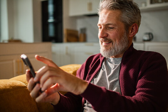 Smiling mature man using smartphone at home