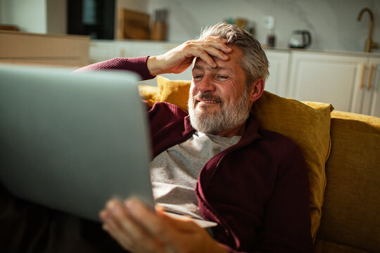 Senior man using laptop and credit card on sofa at home