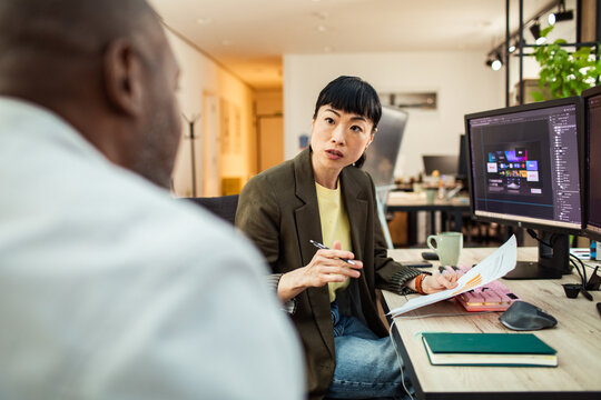 Two coworkers discussing design project at modern office desk