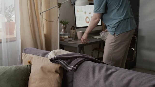 Caucasian young man cleaning computer desk with wet cloth and putting clothes away while doing housework