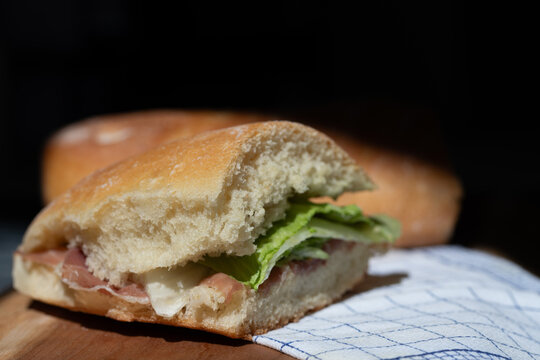 A fresh slice of bread is topped with ham and lettuce. The bread is resting on a wooden board. There is space for text in the background.