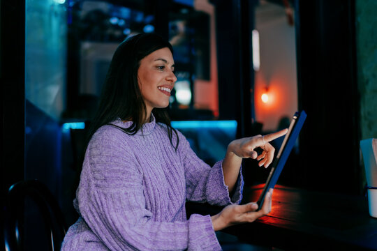 Smiling female user typing on digital tablet with stylus in hand. Financial technology, online banking, data processing or creative editing. Modern professional working in wooden textured office.