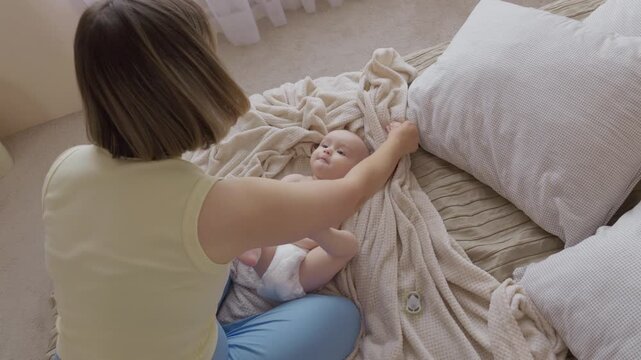 mother massaging baby legs and arms on soft blanket. gentle limb movements and soothing touch with mom and infant. tactile skin and soothing eye contact. motherhood routine in cozy home atmosphere