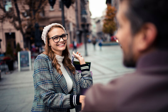 Smiling woman with shopping bags talking on city street in autumn