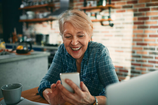 Happy senior woman using smartphone at home kitchen