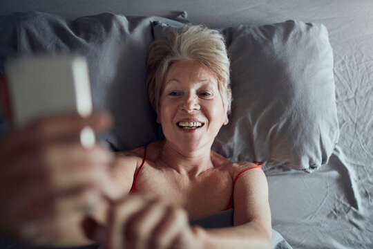 Smiling senior woman taking selfie in bed at home