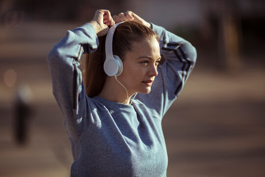 Woman tying hair and wearing headphones before a run outdoors