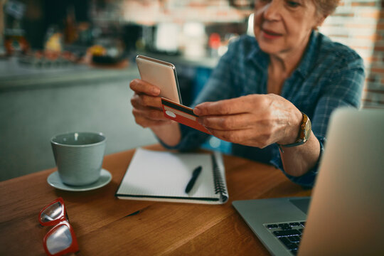 Senior woman using smartphone and credit card at home