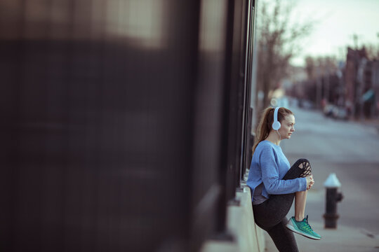 Young woman stretching with headphones on city sidewalk