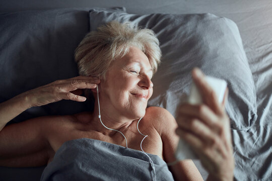 Smiling senior woman listening to music in bed at night