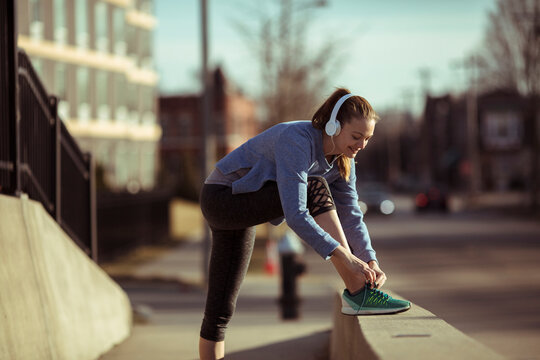 Woman runner tying shoe on city sidewalk with headphones