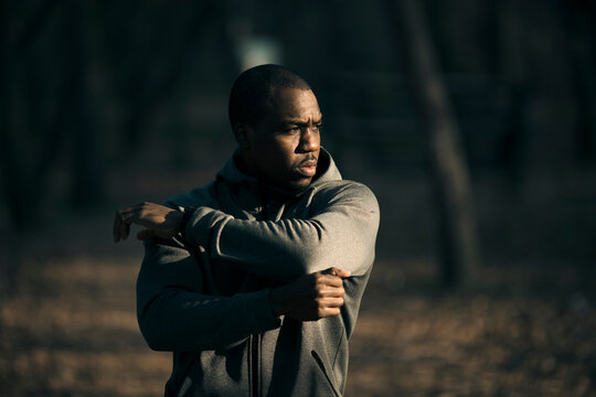 Focused man stretching before run in forest park at sunrise