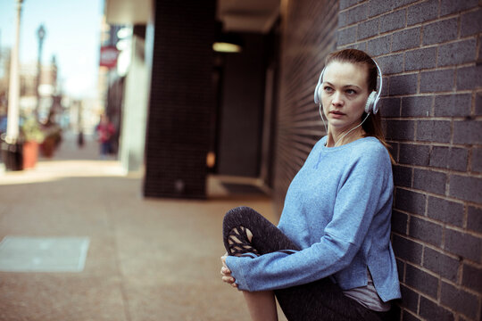 Woman in headphones stretching on urban sidewalk