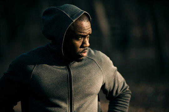Focused male runner resting in hoodie outdoors at dusk