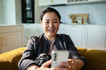 Smiling woman using smartphone at home on sofa