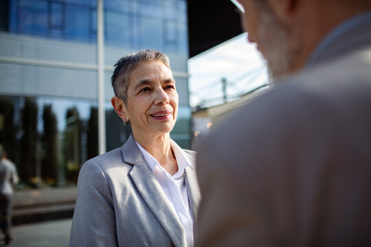 Senior businesswoman talking with colleague outside office building