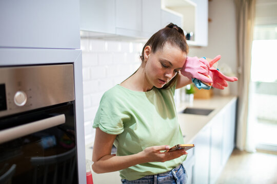 Woman checking phone while cleaning kitchen at home