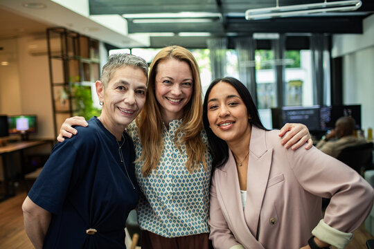 Three diverse female colleagues smiling together in modern office