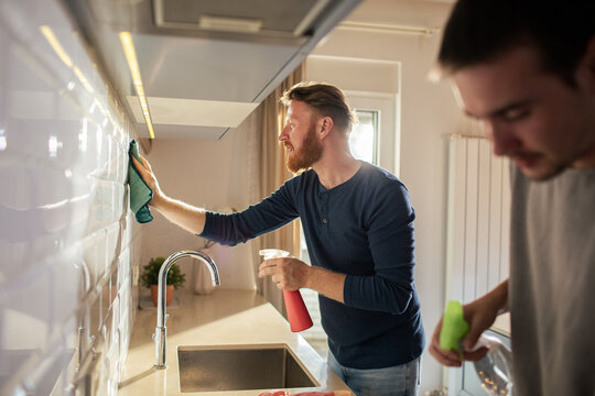 Two men cleaning kitchen backsplash at home